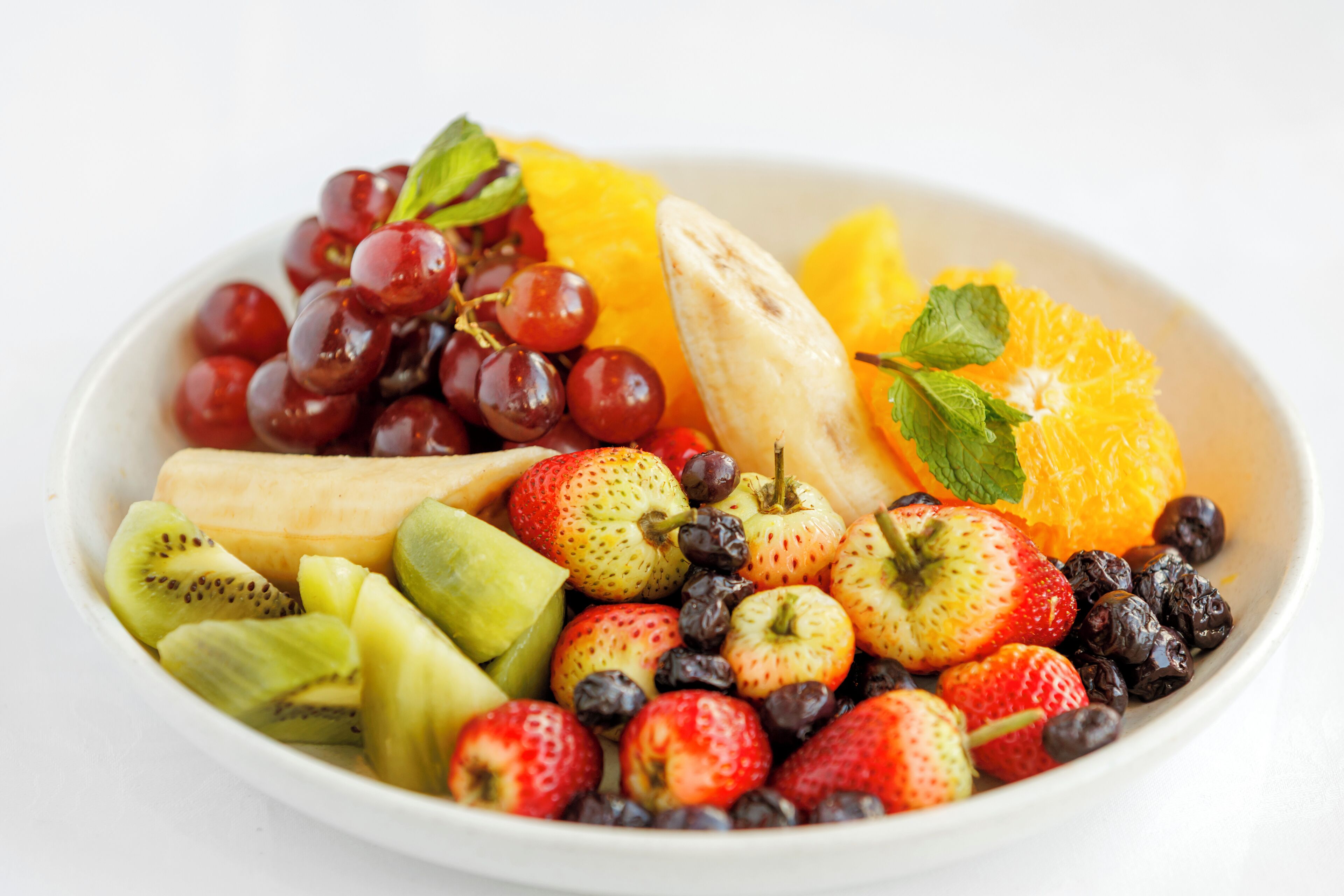 Un saladier rempli d’un assortiment de fruits, notamment des raisins, des fraises, des kiwis et des bananes.