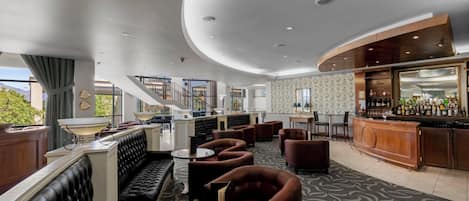 A modern lounge area with a bar, seating arrangements, and a staircase leading to an upper level.