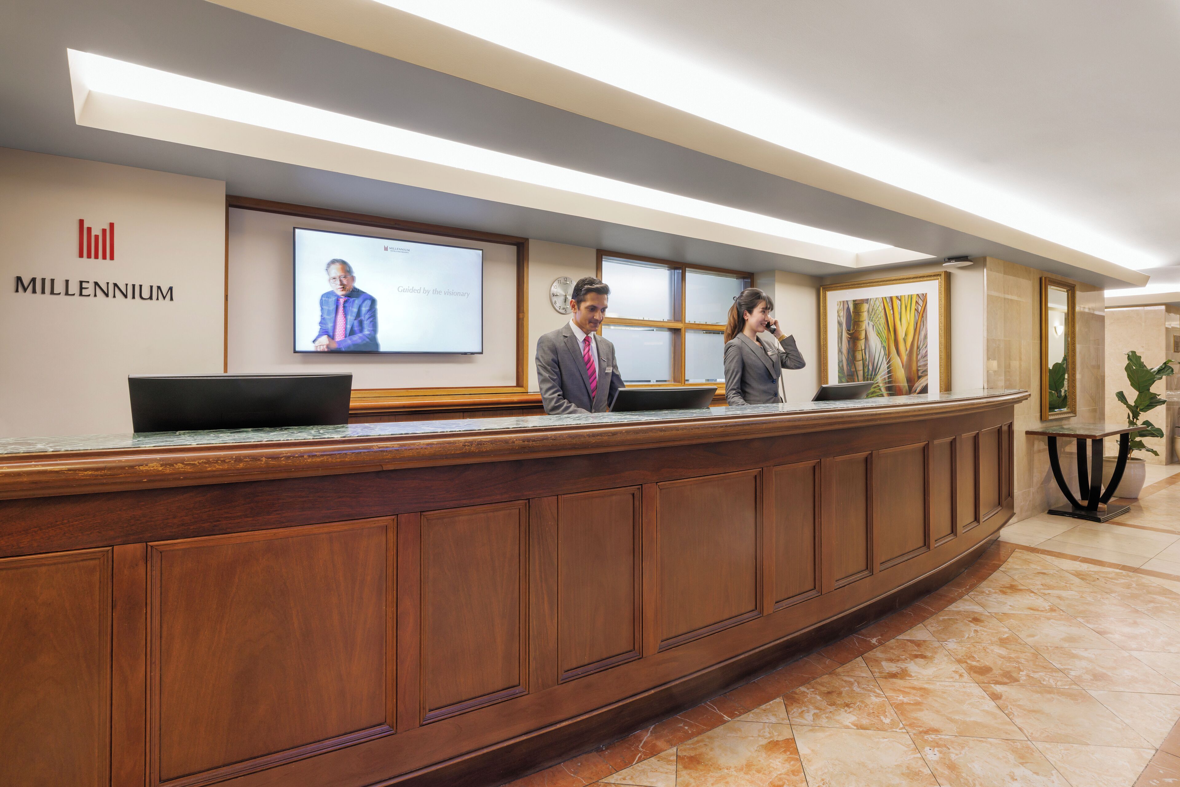 Un mostrador de recepción con detalles de madera, una pantalla digital mostrando una presentación y el logotipo de 'Millennium'.