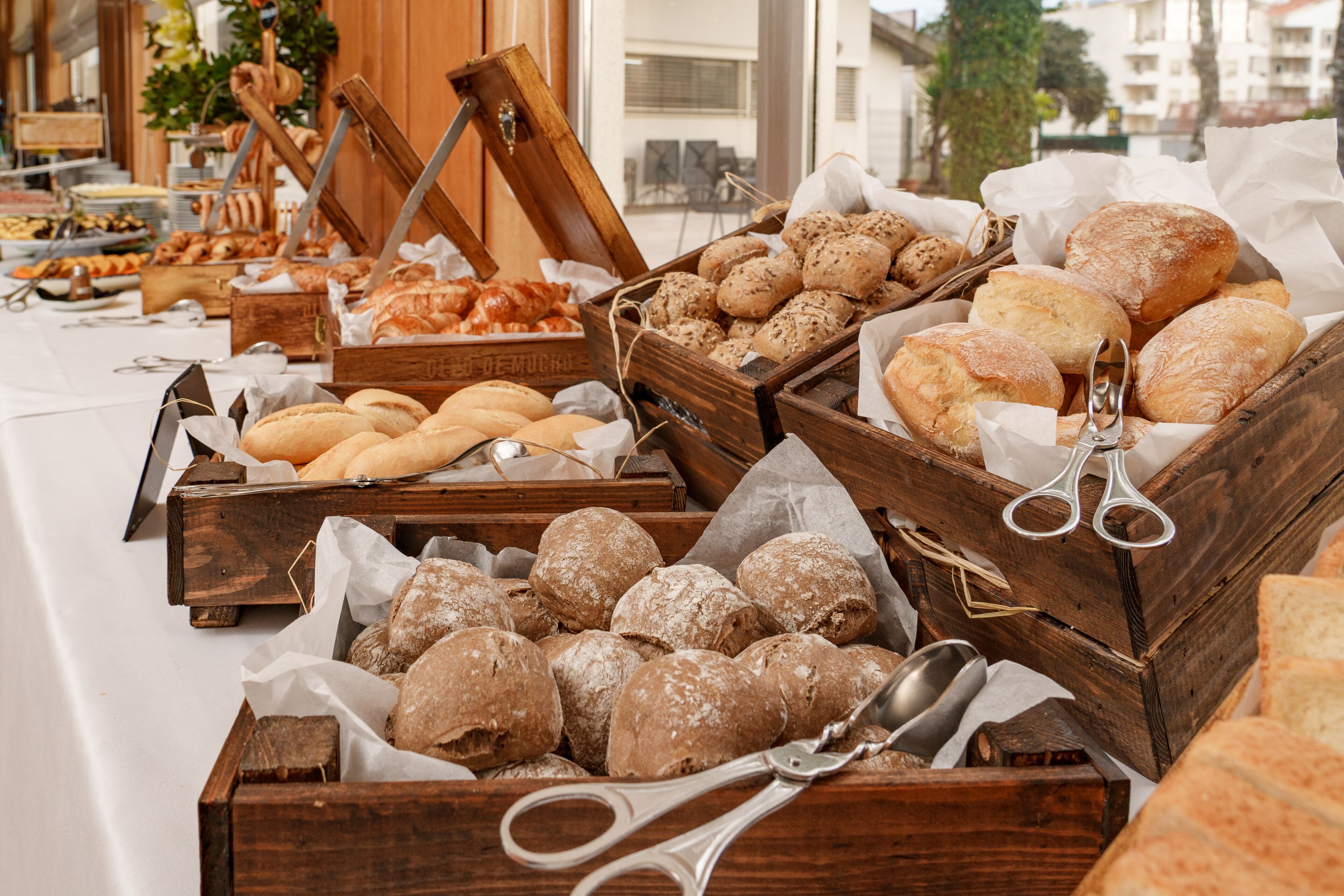 A variety of baked goods displayed in wooden crates on a table, with a pair of scissors and spoons nearby.