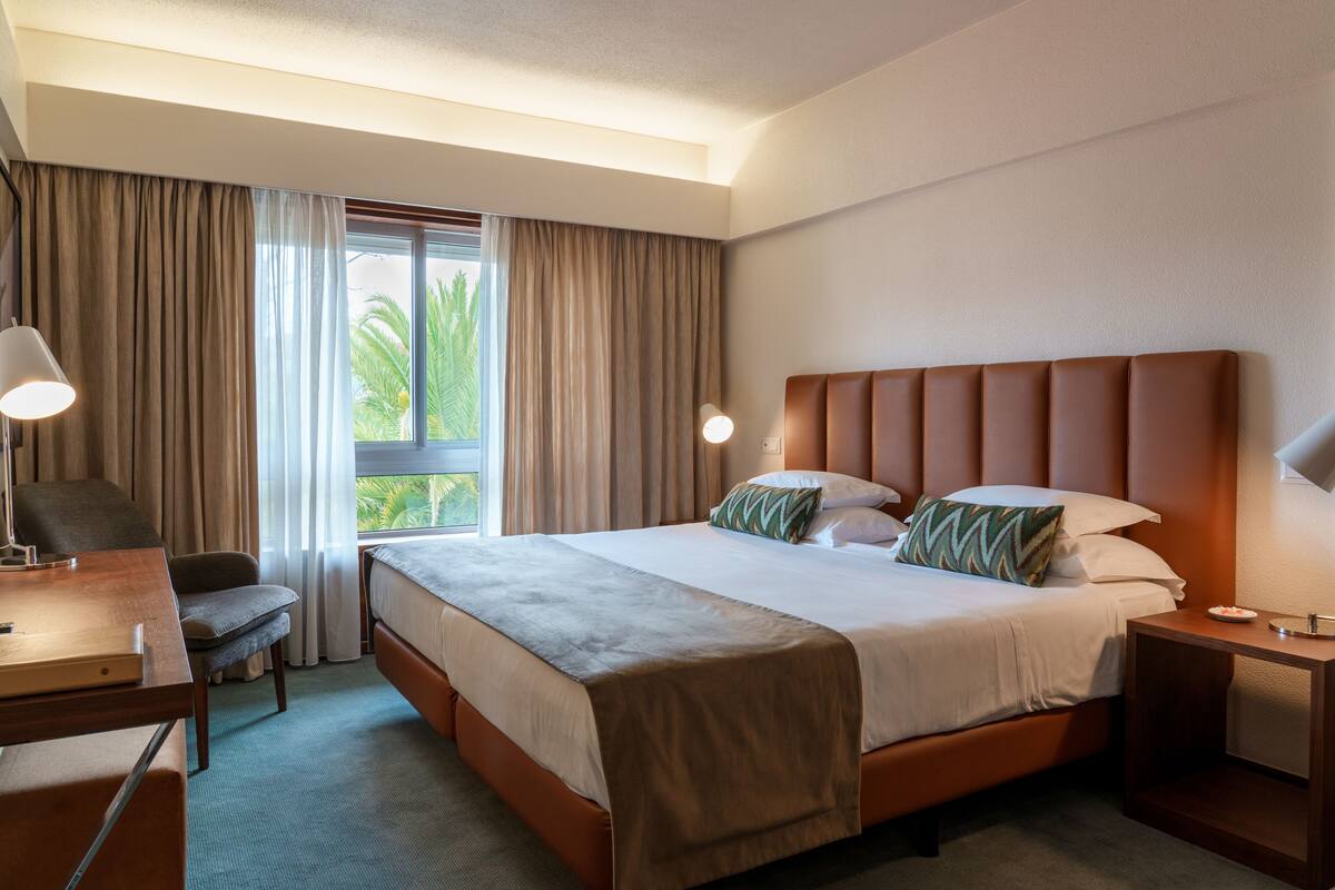 A hotel room with a large bed, a desk, a chair, and a window with curtains.