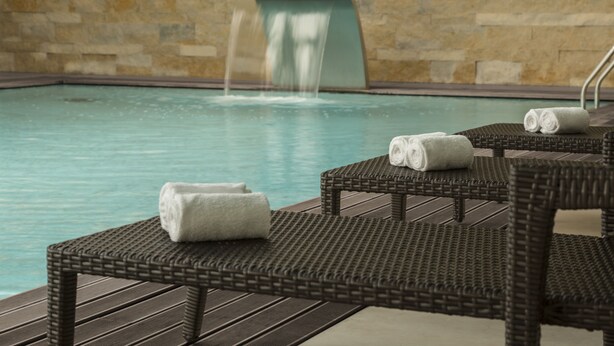 A pool area with a waterfall feature, wicker lounge chairs, and towels. - Dom Goncalo Hotel & Spa (Ourem)