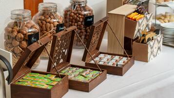 Una mesa de buffet con diversos alimentos, incluyendo frascos de frutos secos y cajas de pasteles.