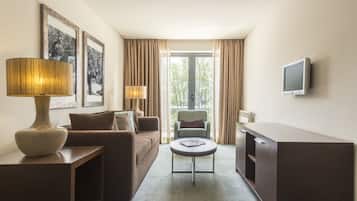 A hotel room with a sofa, a small round table, a lamp, a television, and a window with curtains.