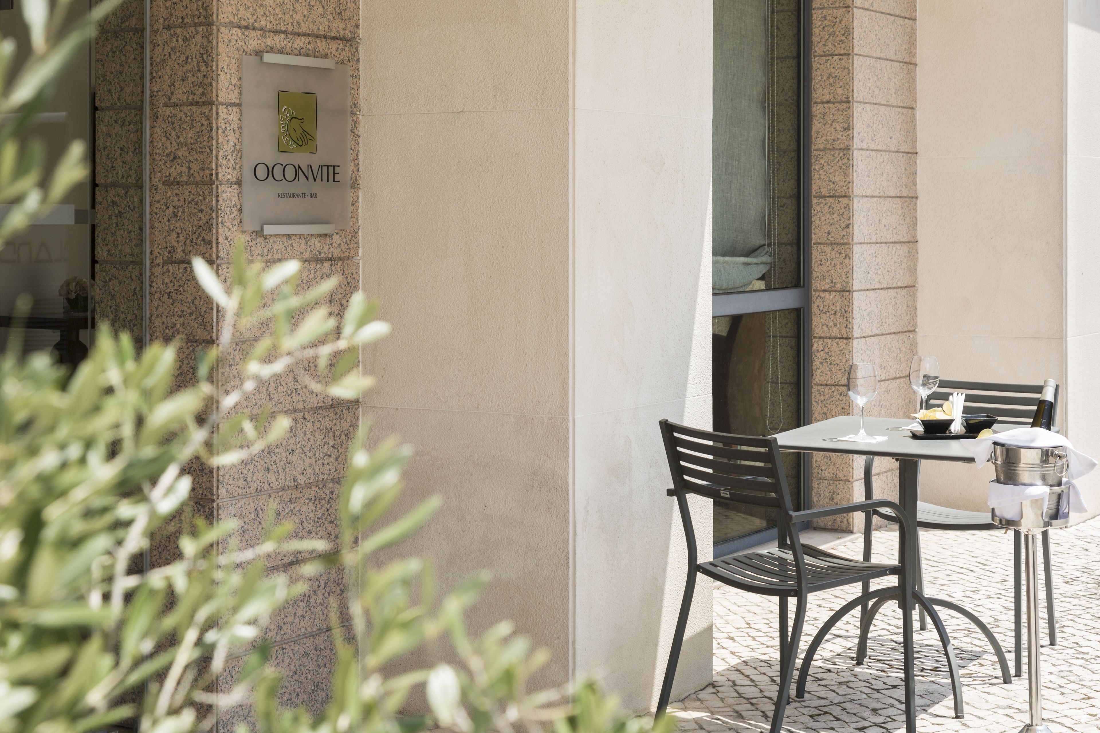 Un espacio al aire libre con mesas y sillas, un letrero del restaurante 'O'Convite' y una botella de champán.