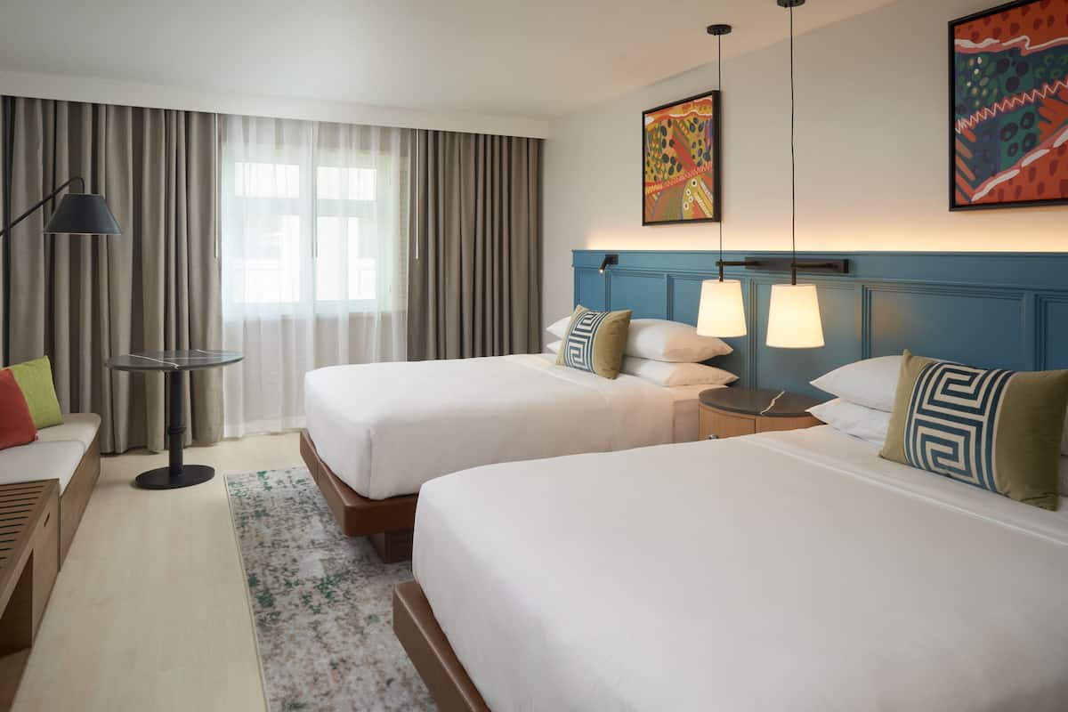 Une chambre d’hôtel avec deux lits, un bureau, une lampe et des œuvres d’art accrochées aux murs.