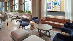 A modern hotel lobby with a seating area, tables, and a large window with a view.
