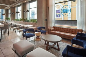 Un hall d’hôtel moderne, doté d’un espace salon, de tables et d’une grande fenêtre offrant une vue panoramique.