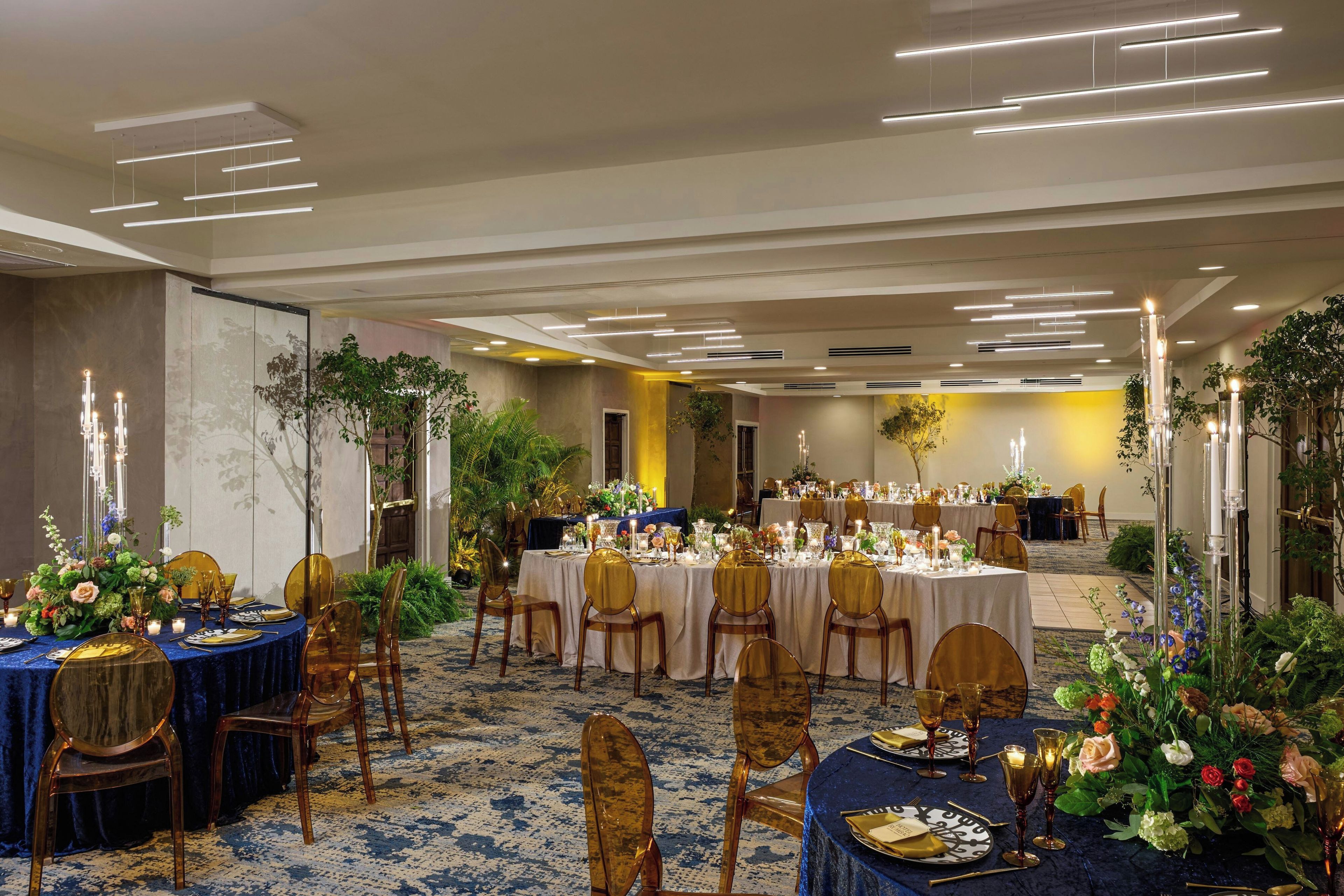 Une salle de banquet avec des tables rondes, des chaises dorées et des centres de table floraux.