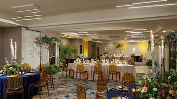 Une salle de banquet avec des tables rondes, des chaises dorées et des centres de table floraux.
