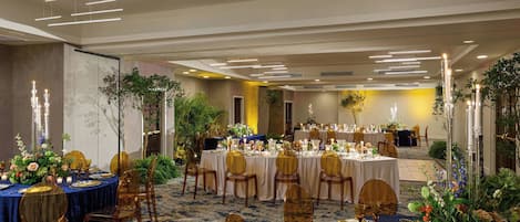 Un salón de banquetes con mesas redondas, sillas doradas y centros de mesa florales.