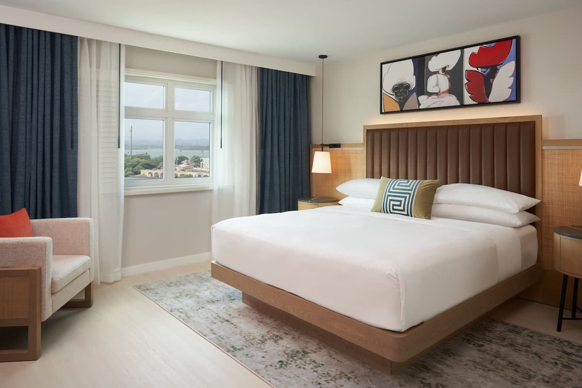Une chambre d’hôtel avec un grand lit, une chaise, une table de chevet, une lampe et un tableau au mur.