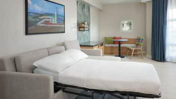 Une chambre d’hôtel avec un lit, un canapé, une petite table et une chaise. Il y a un tableau au mur et une fenêtre avec des rideaux.