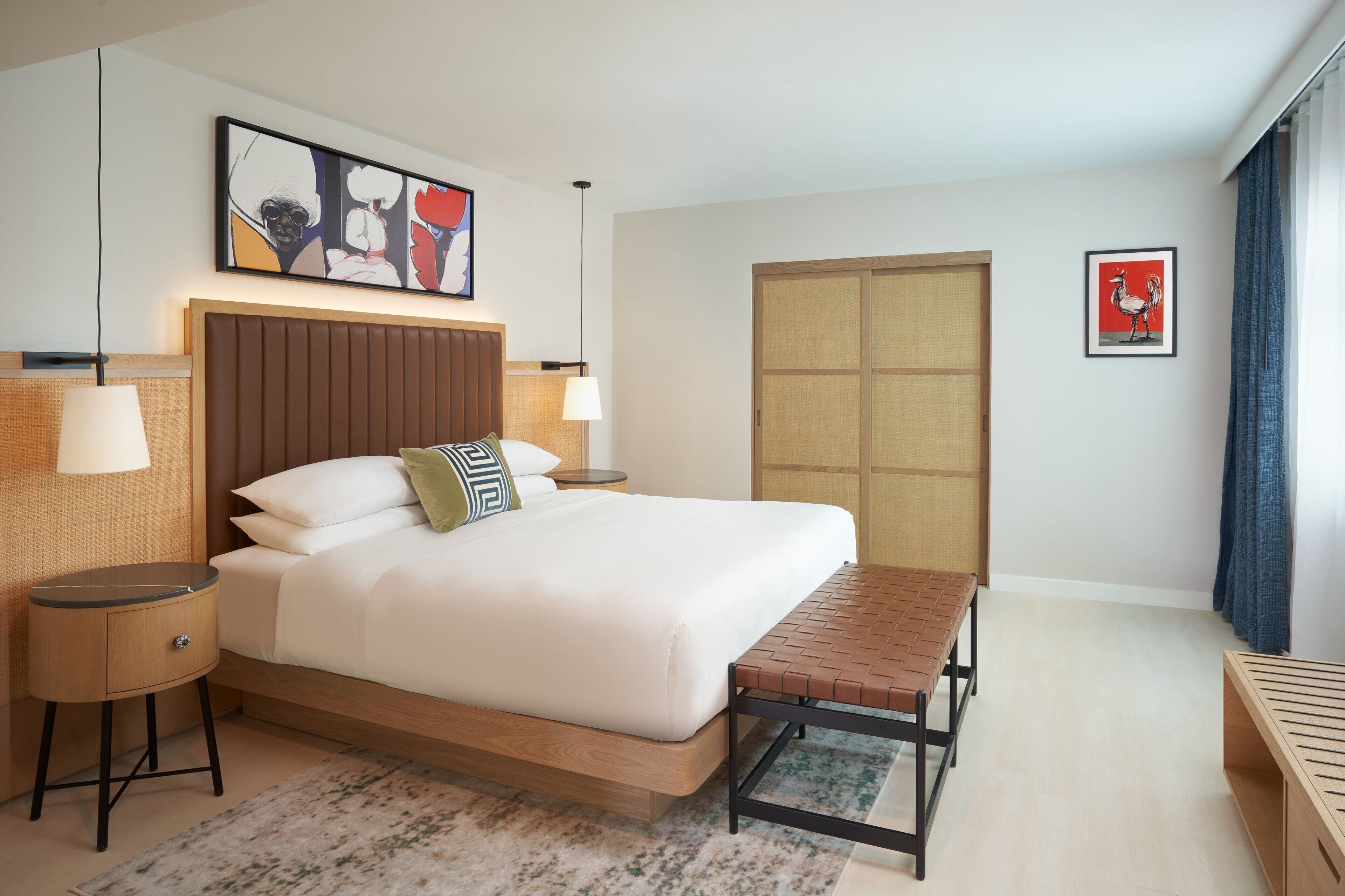 A modern hotel room with a large bed, bedside tables, a bench, and artwork on the walls.