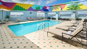 A pool area with a view of the city skyline, lounge chairs, and a colorful mural on the ceiling.