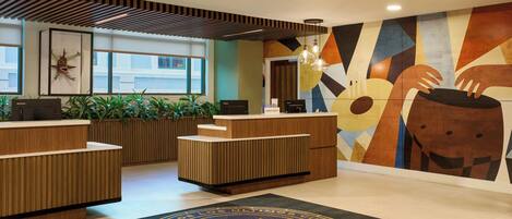A hotel reception area with a modern design, including a wooden reception desk, a large wall mural, and a doormat with a circular emblem.