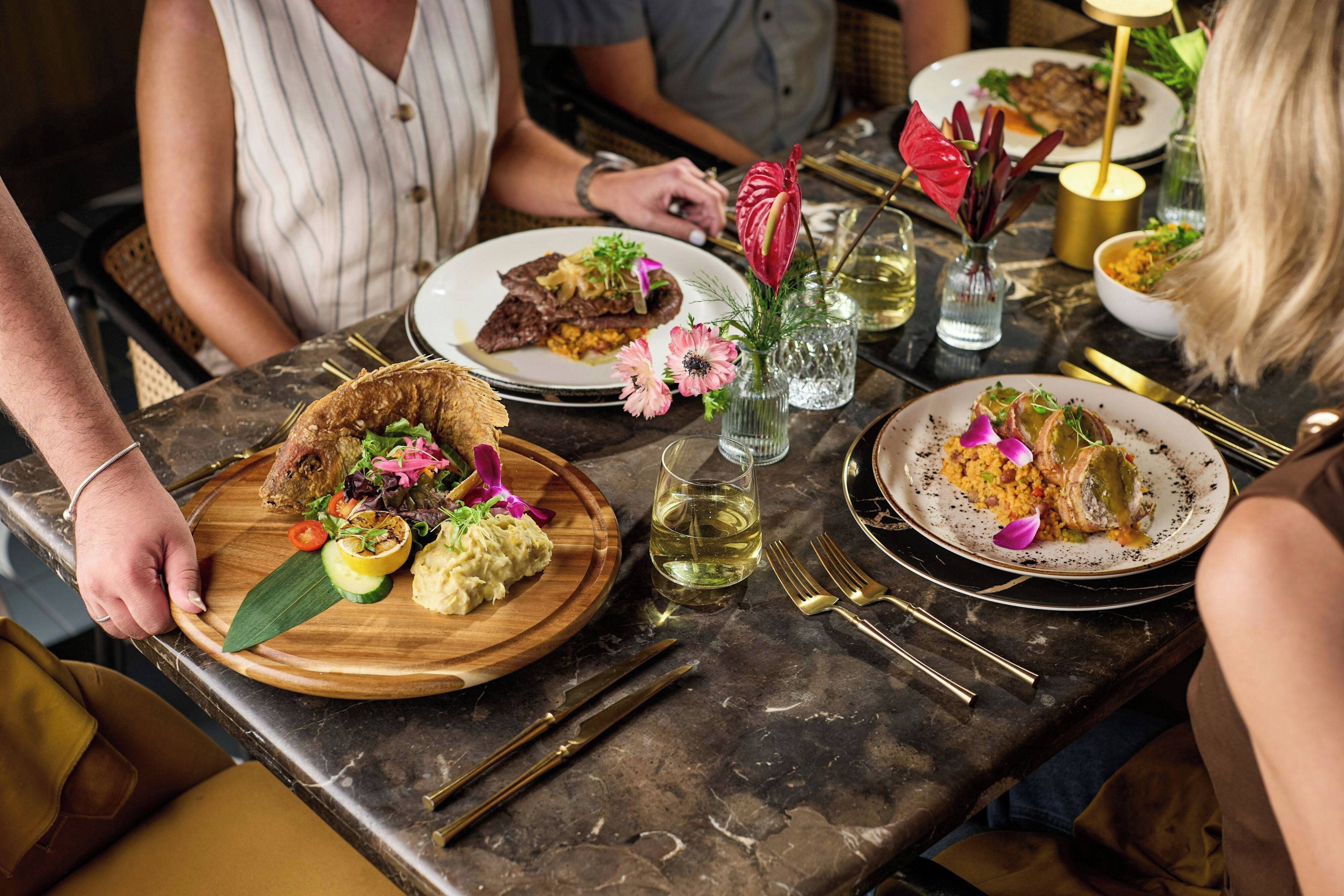 A dining table with various dishes, including a plate with a grilled item, a bowl of rice, and a glass of white wine.