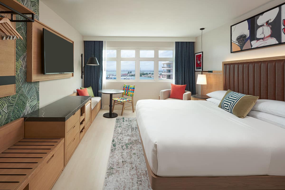 Une chambre d’hôtel avec un lit, un bureau, une chaise, une télévision et une fenêtre donnant sur un beau paysage.