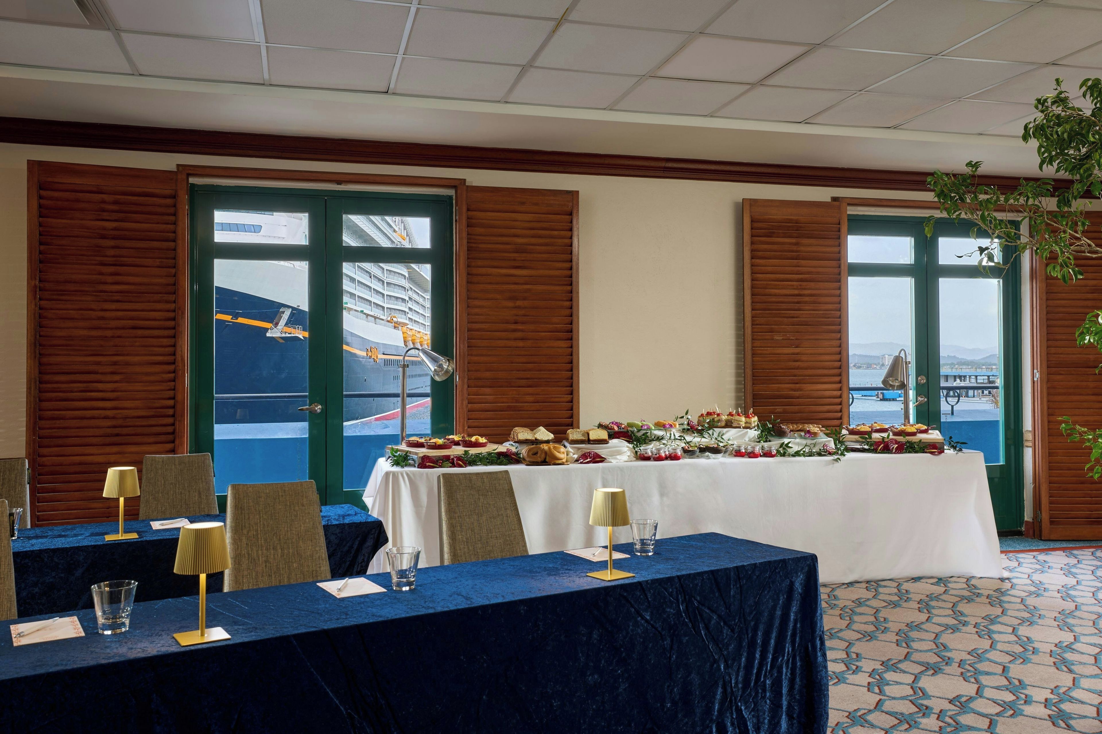 A conference room with a long table set for a meeting, featuring a view of a cruise ship through the windows.