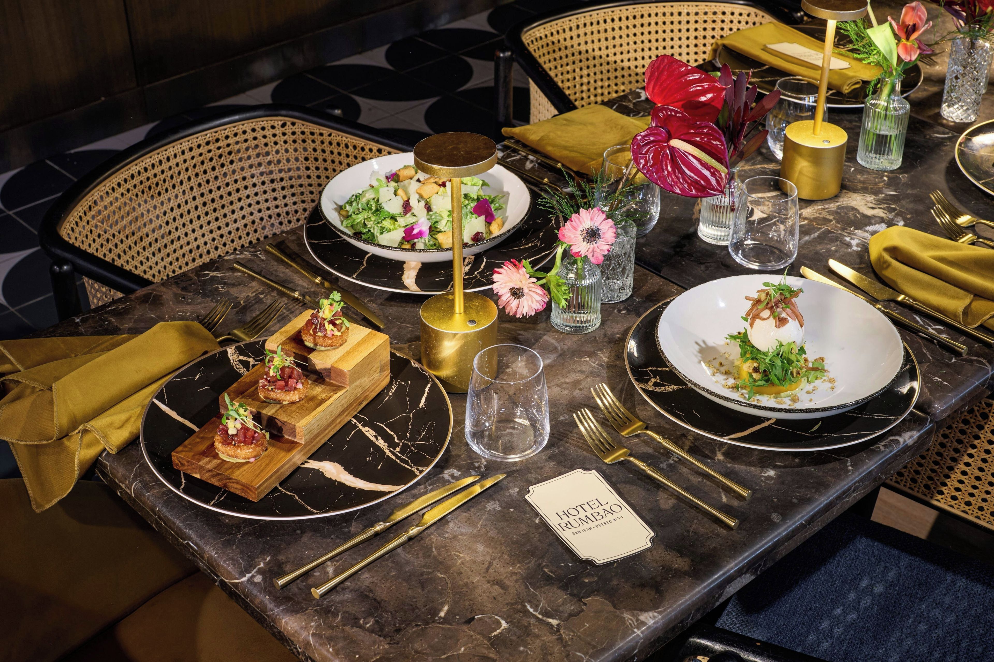 A dining table set with plates, cutlery, and glasses, with a placemat labeled 'HOTEL RUMBAO'.