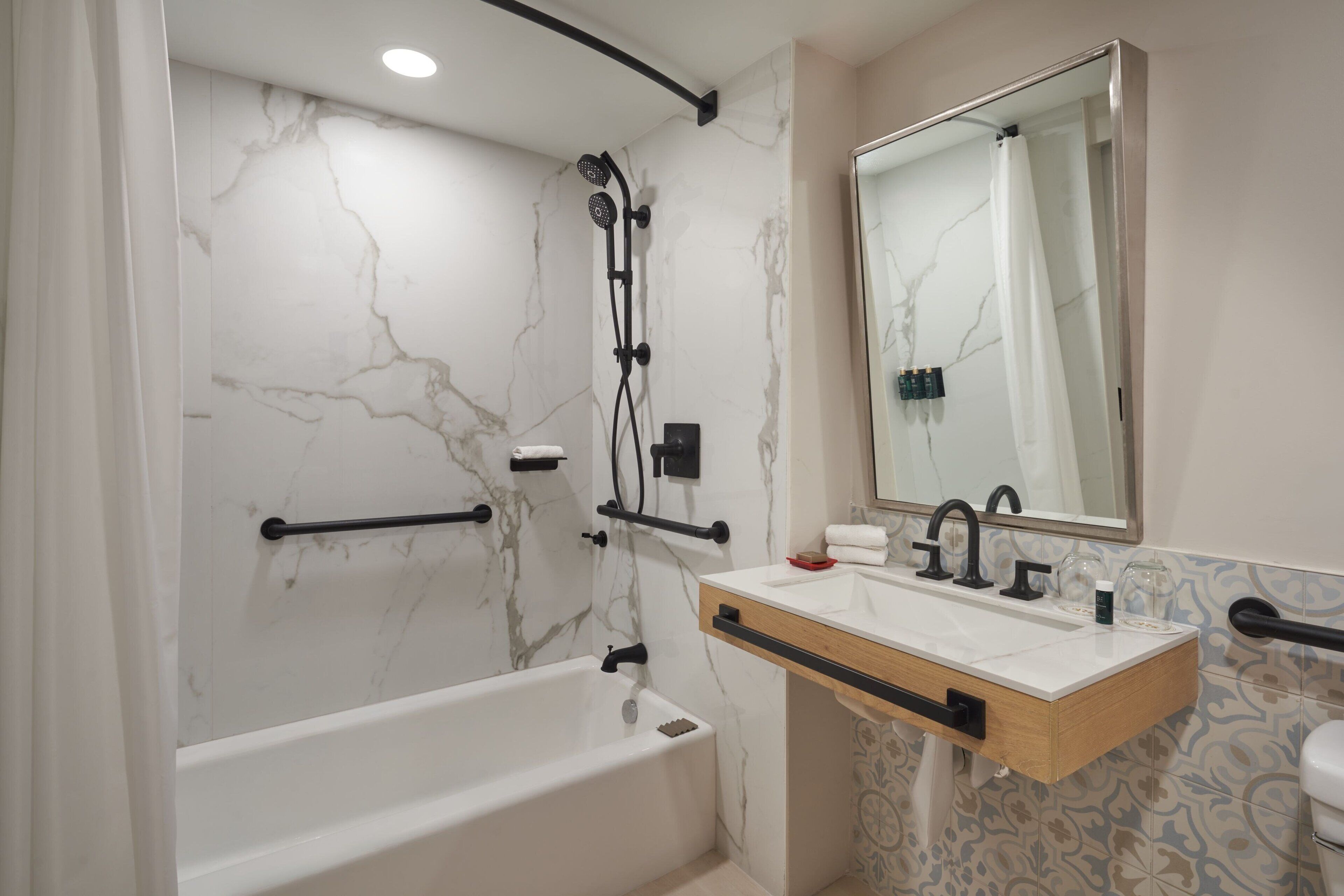 A modern bathroom with a marble wall, a bathtub, a sink with a mirror, and a shower with a handheld showerhead.