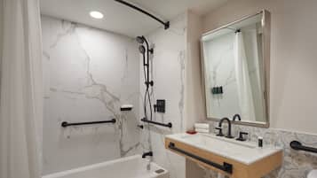 A modern bathroom with a marble wall, a bathtub, a sink with a mirror, and a shower with a handheld showerhead.