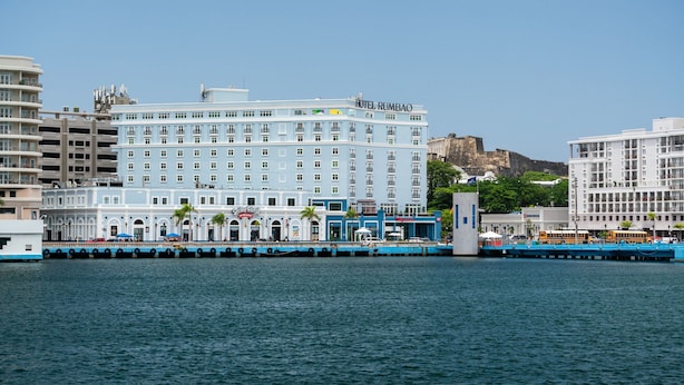 A waterfront hotel with multiple floors, a prominent sign, and a view of the sea.
