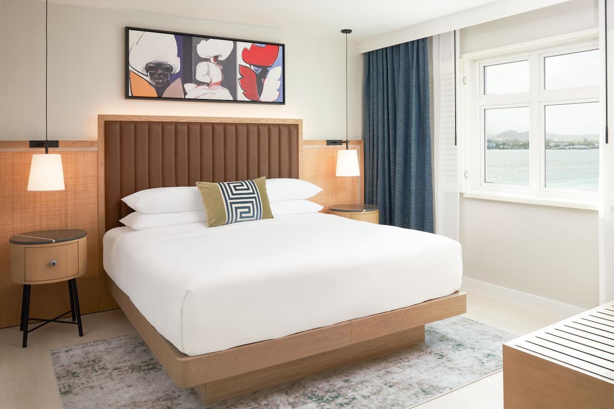 Une chambre d’hôtel moderne avec un grand lit, deux tables de chevet, une fenêtre donnant sur un beau paysage et un tableau au mur.