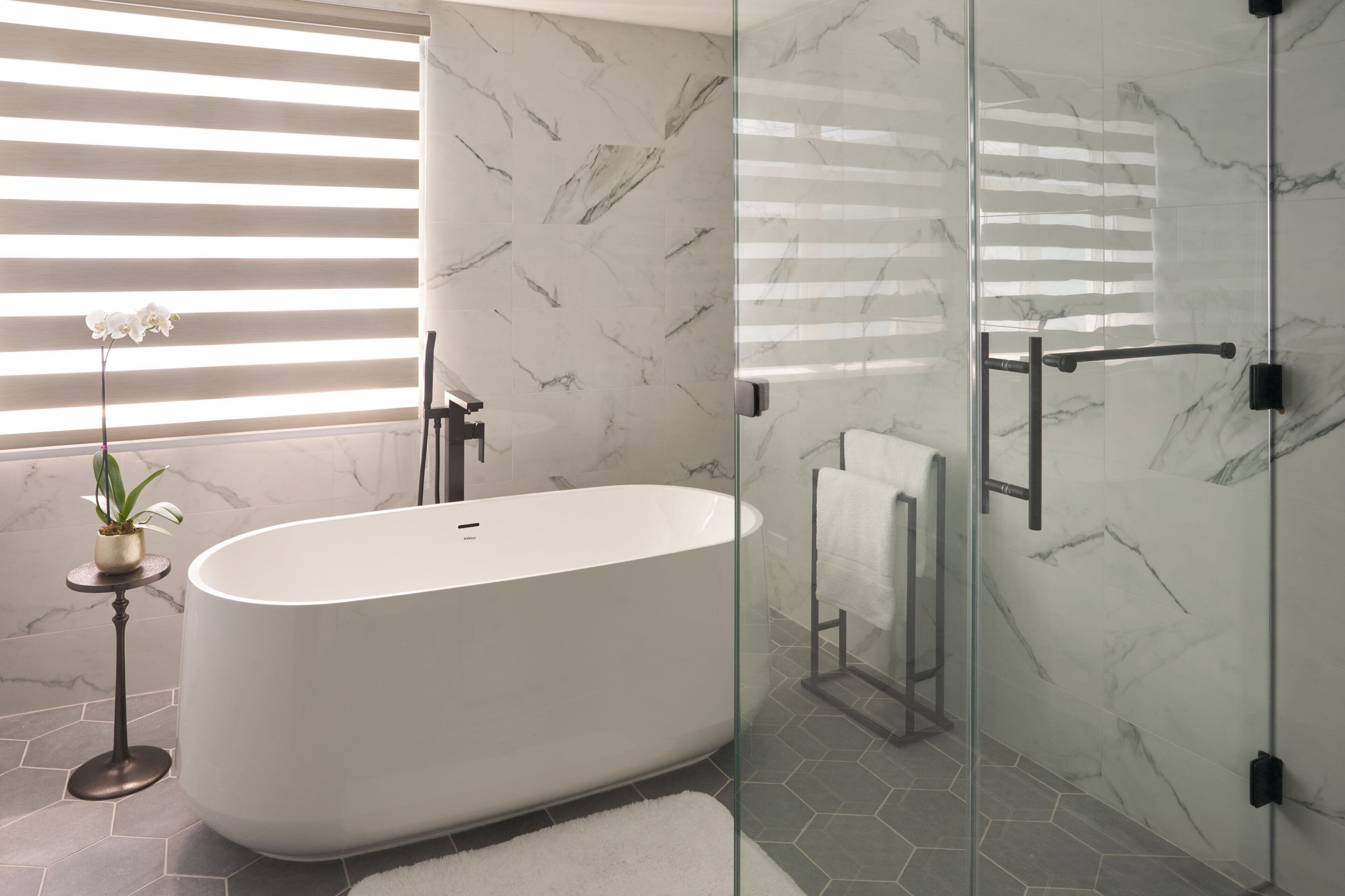 A modern bathroom with a freestanding bathtub, glass shower enclosure, and marble walls.
