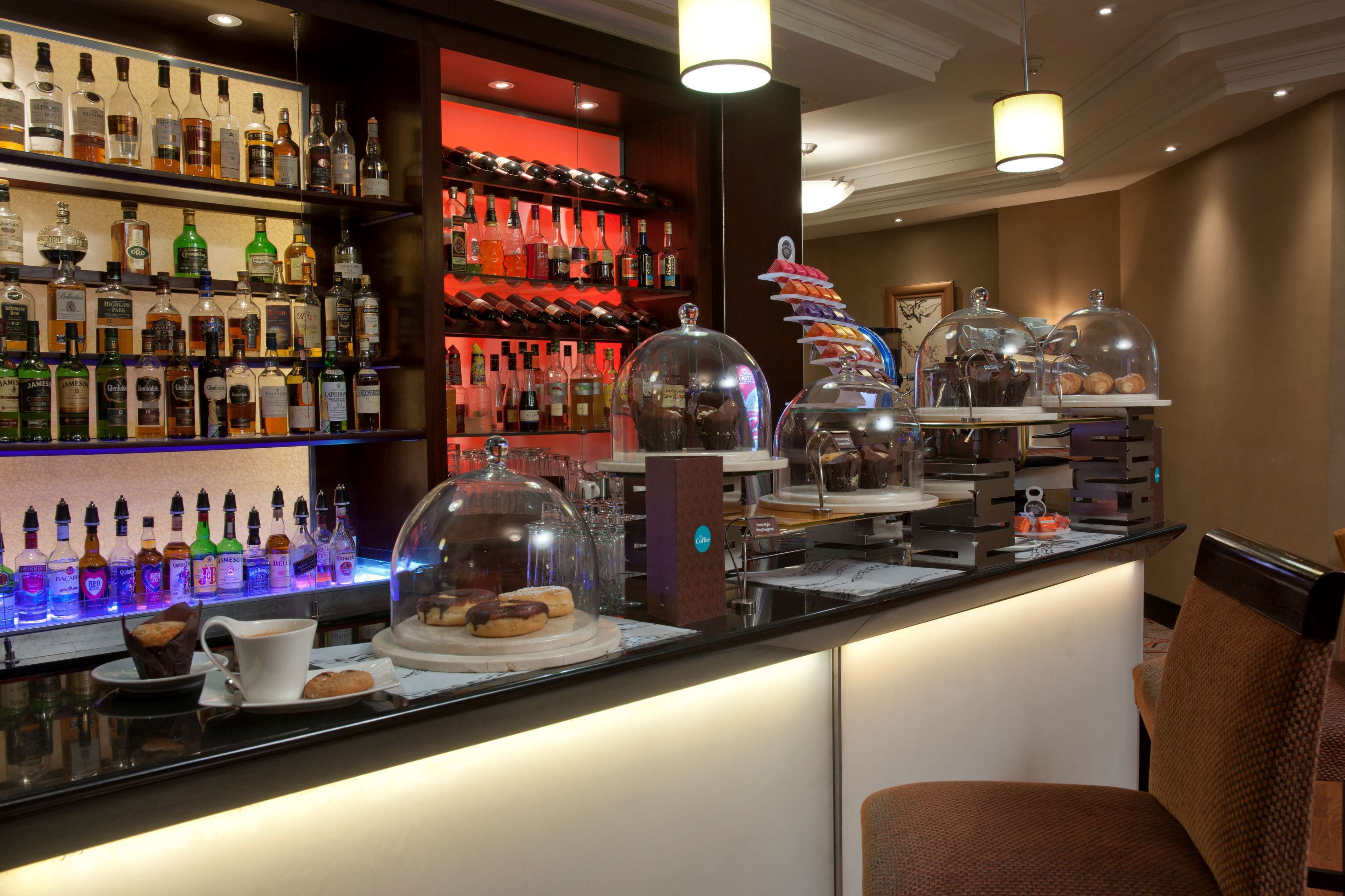 Zona de bar con estantes llenos de botellas de licor, una estación de café y un área de descanso con sillas.