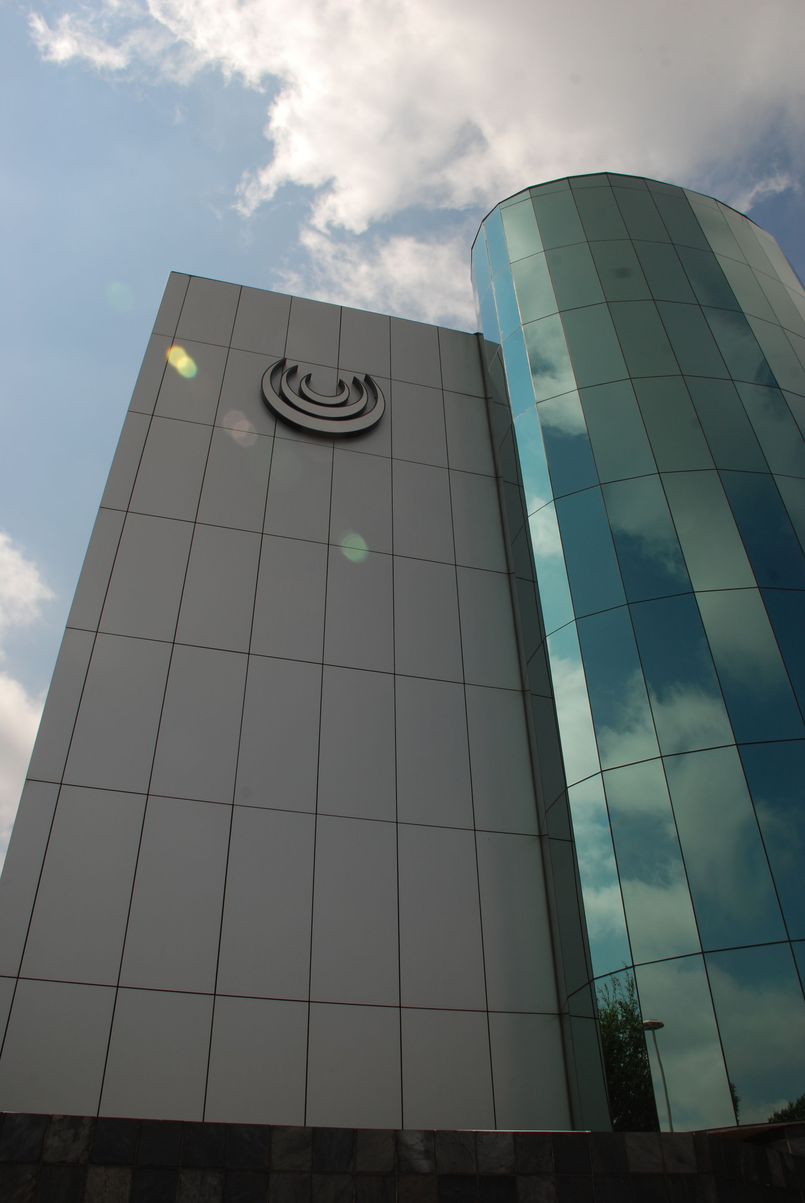 A modern building with a reflective glass facade and a distinctive logo on the front.