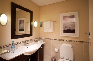 Un baño con lavamanos, espejo, toallero y retrete.