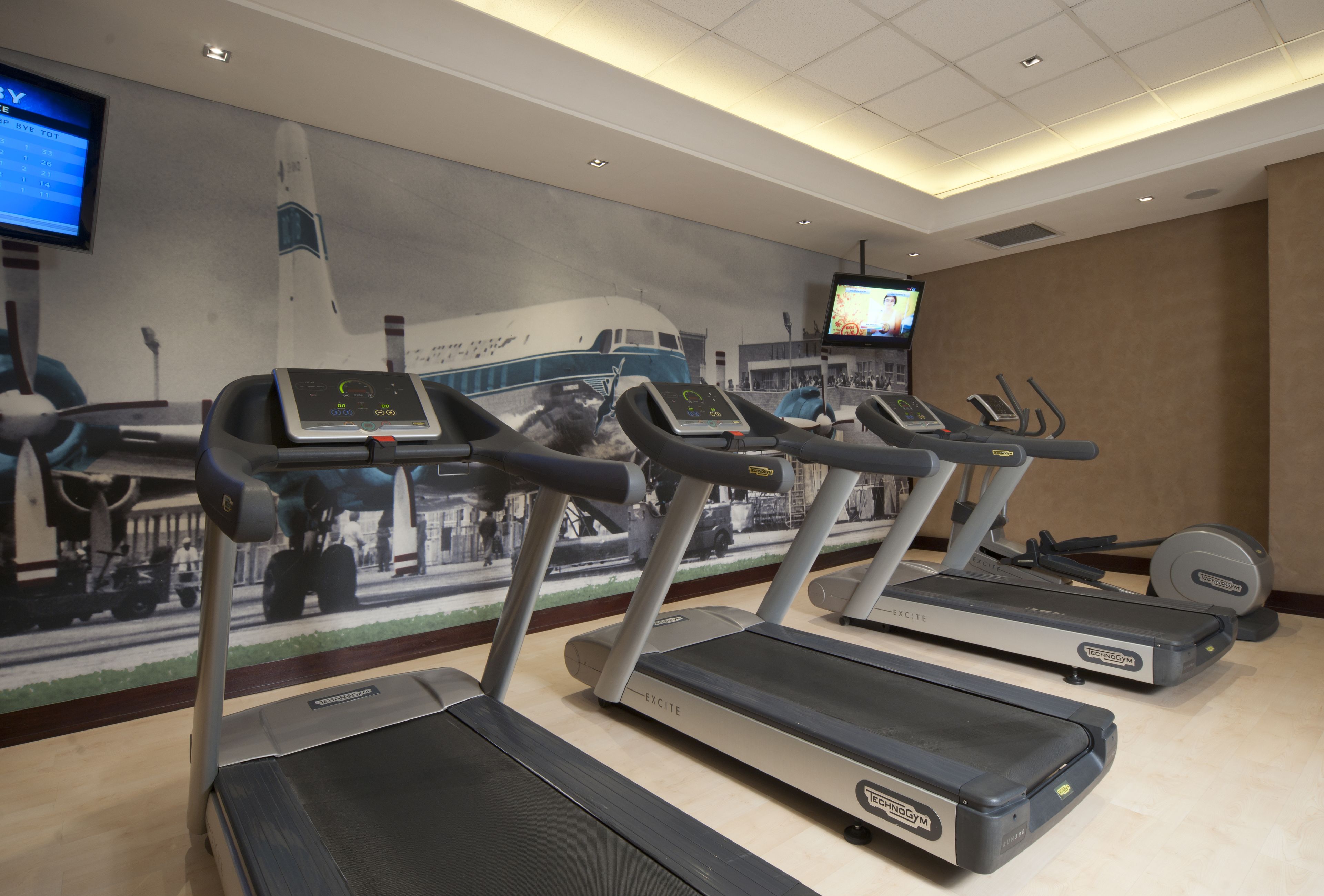 Een fitnessruimte met loopbanden, een hometrainer en een televisiescherm.