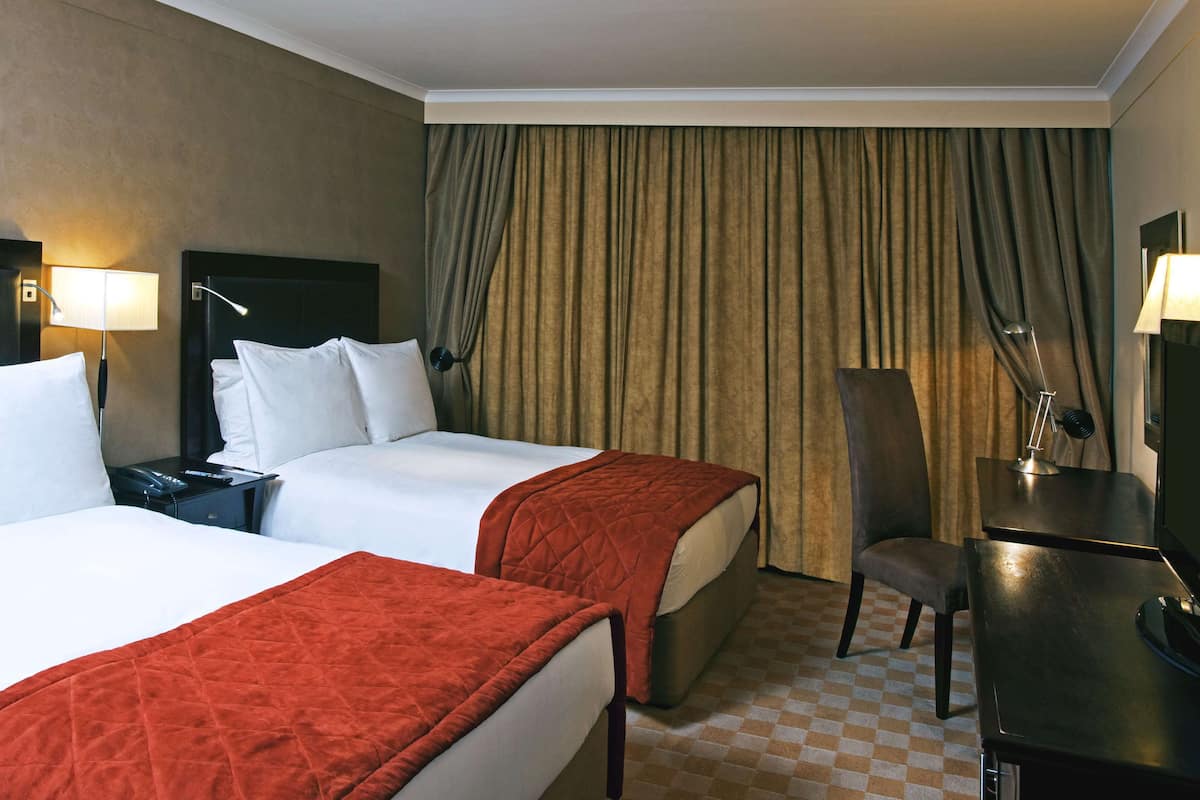 A hotel room with two beds, a desk, a chair, and a checkered floor.