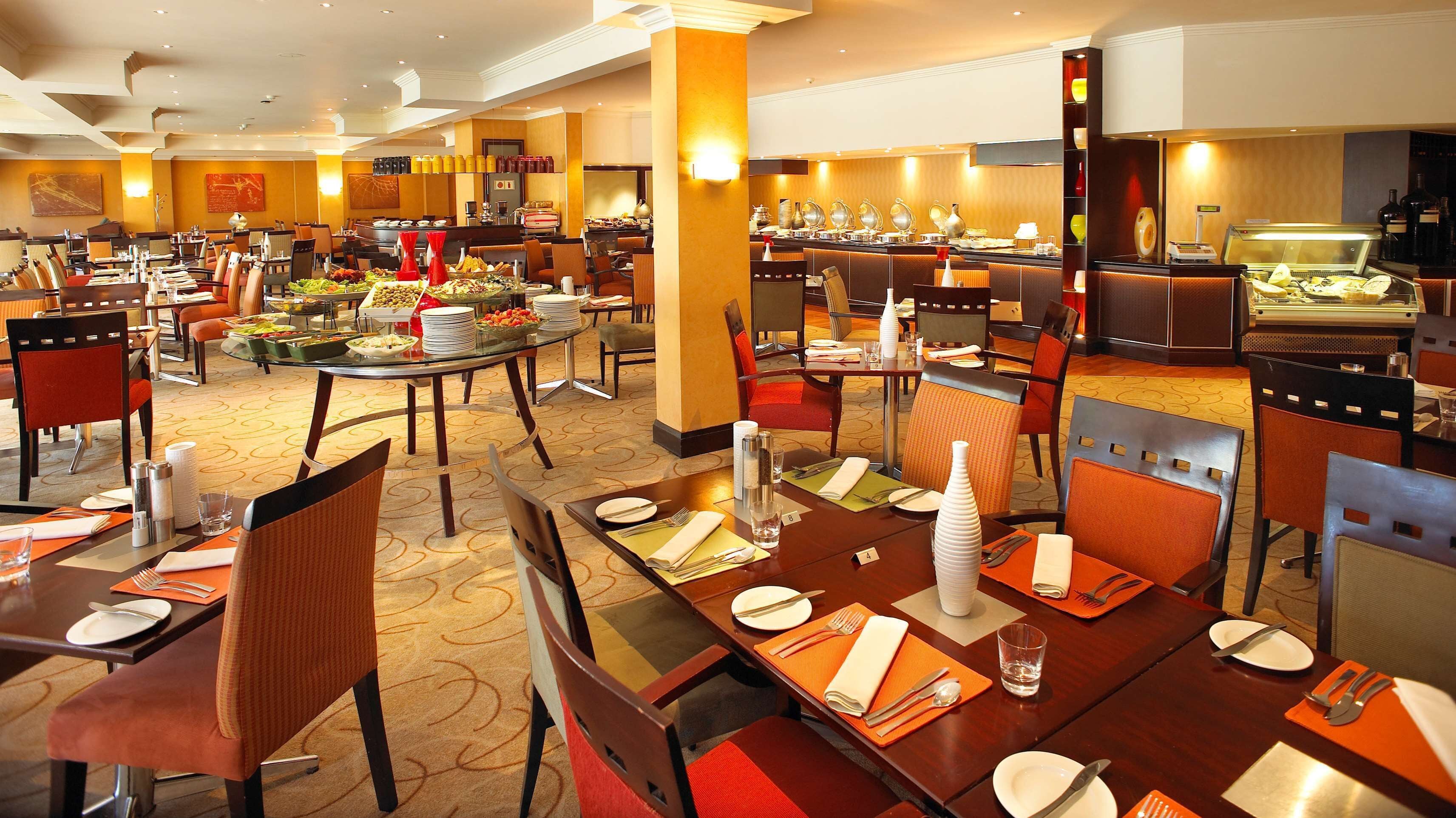 Un comedor de hotel con varias mesas dispuestas para los huéspedes, provistas de platos, cubiertos y vasos.