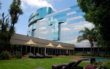A hotel with a modern glass facade, outdoor seating area with umbrellas, and a pool.