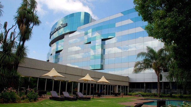 Un hotel con fachada de vidrio moderna, zona de estar exterior con sombrillas y piscina.