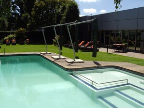 A swimming pool with a tiled deck, lounge chairs, and a covered seating area. - Southern Sun O.R Tambo (Kempton Park)