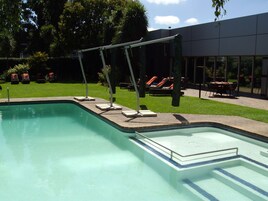 Una piscina con un bordeado de baldosas, sillas de descanso y un área de estar techada.