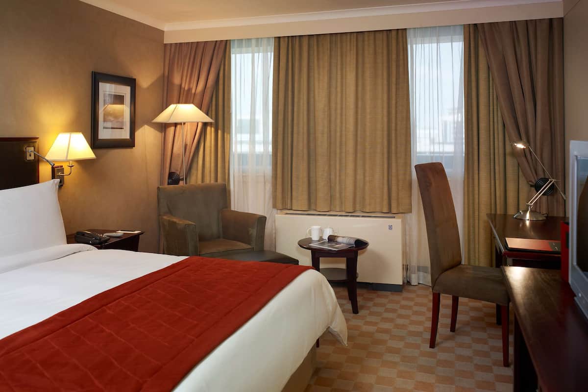 A hotel room with a bed, a desk, a chair, a lamp, and a window with curtains.