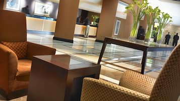Un hall d’hôtel avec des fauteuils à motifs à carreaux, un comptoir d’accueil et une table basse en verre.