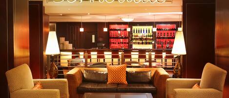A lobby with a bar area, leather sofas, patterned armchairs, and a carpeted floor.