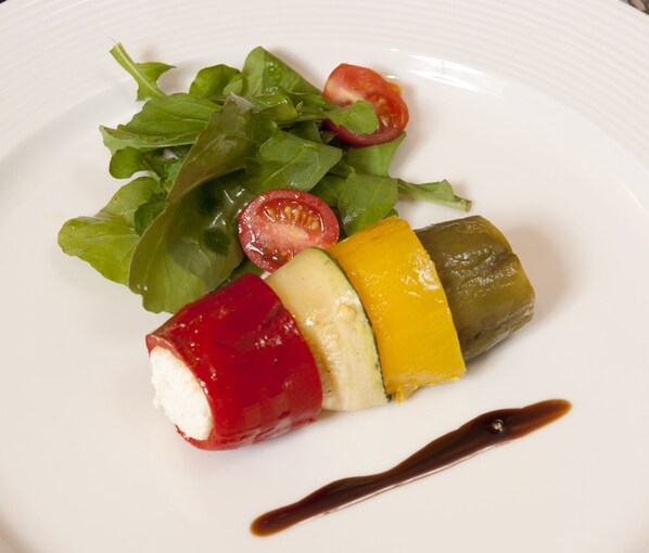 A plate with a salad, a stuffed pepper, and a drizzle of sauce.