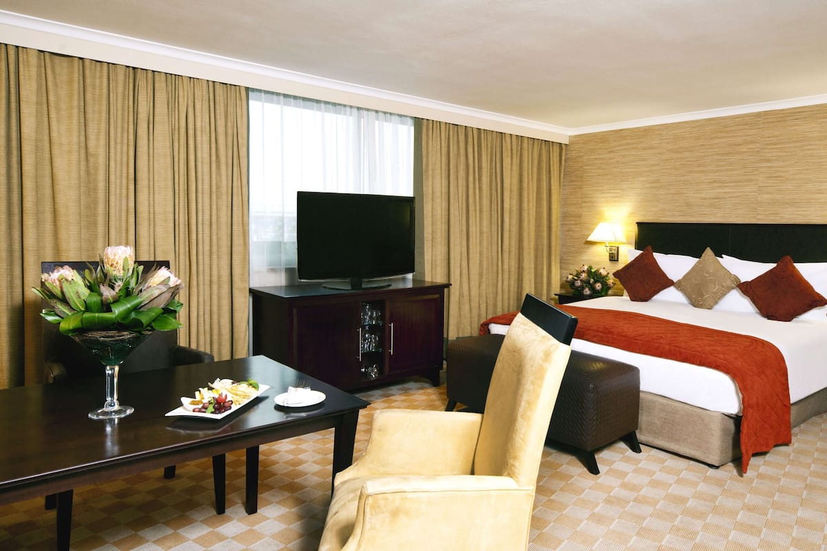 A hotel room with a bed, a television, a dining table with a vase of flowers, and a chair.