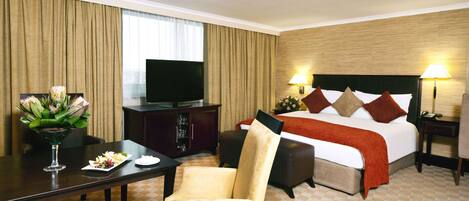 Habitación de hotel con cama, televisión, mesa de comedor y un florero, además de una silla.