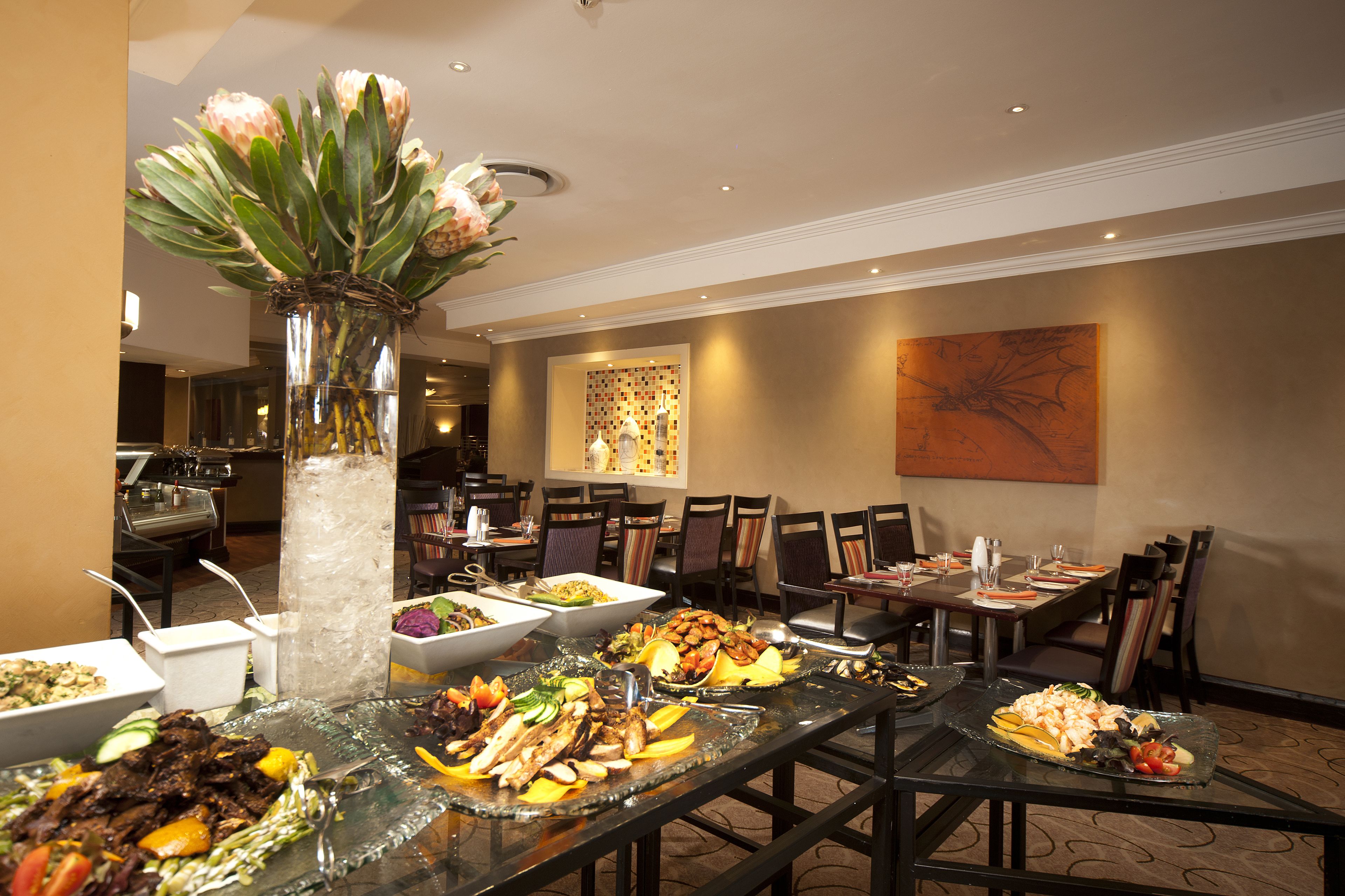 Un buffet proposant divers plats, un vase décoratif avec des fleurs et un espace repas avec des chaises et des tables.