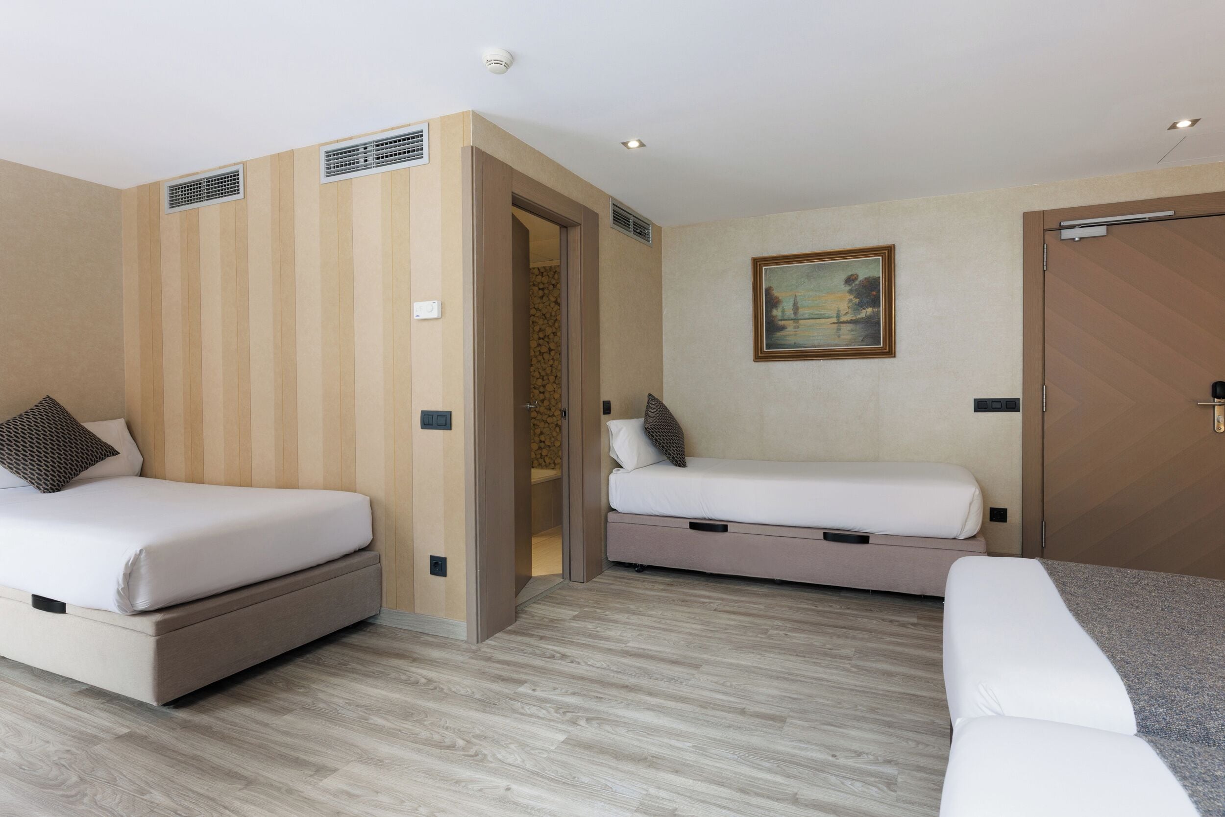 A hotel room with two beds, a painting on the wall, and a wooden door.