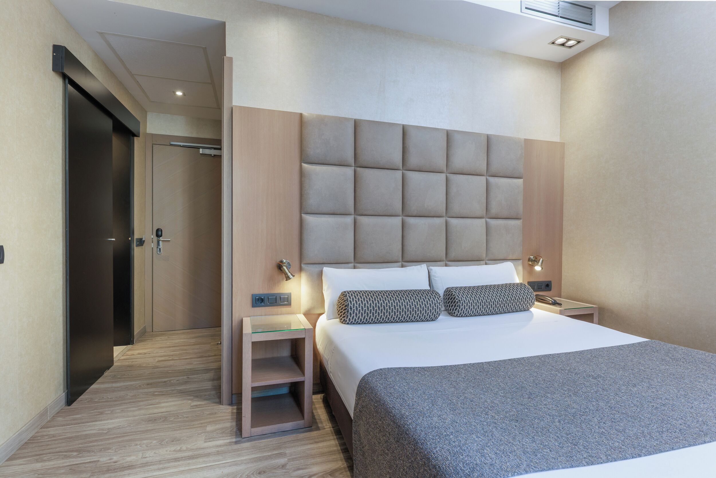 Una habitación de hotel moderna con una cama grande, una mesita de noche y un armario.