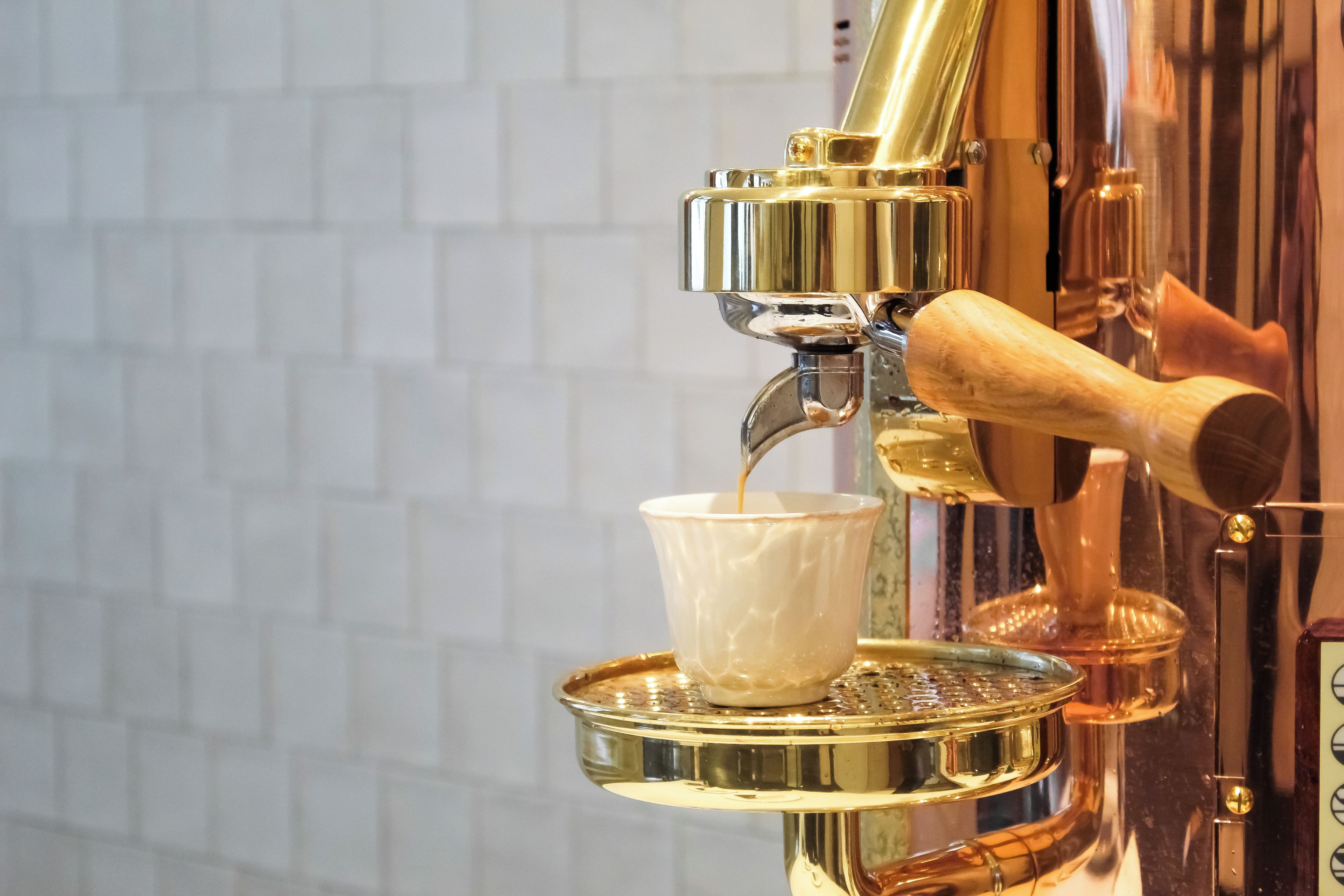 A coffee machine with a cup placed under the spout, a metallic tray, and a wooden handle.