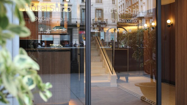 A hotel interior with a reception desk, a staircase, and a view of the street outside. - Hotel Suizo (Barcelona)